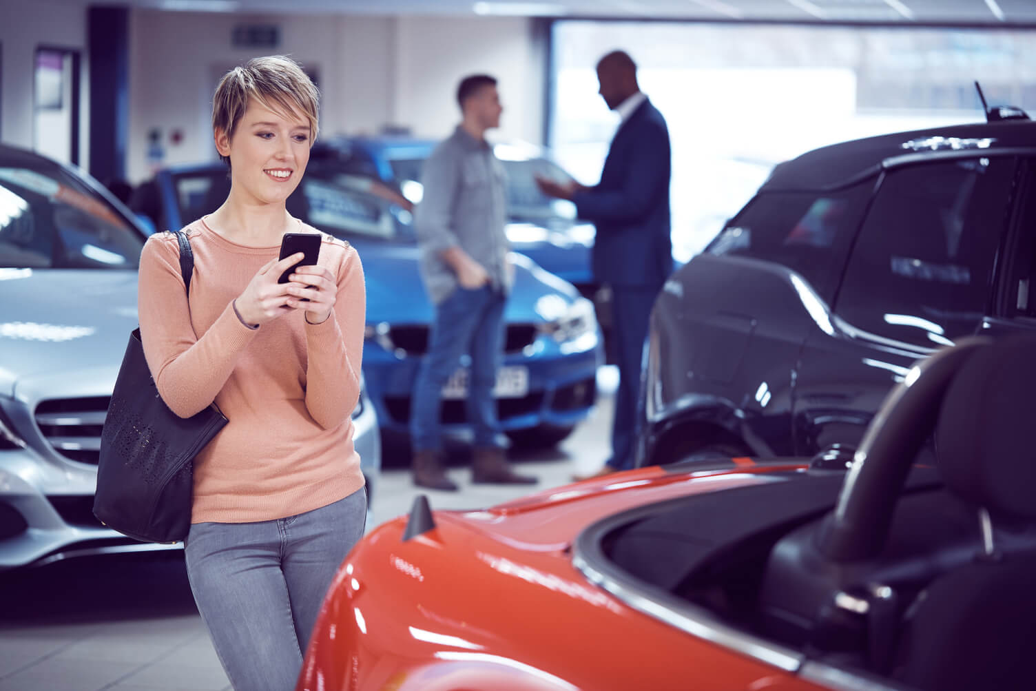 Lady taking picture of new car on showroom floor.